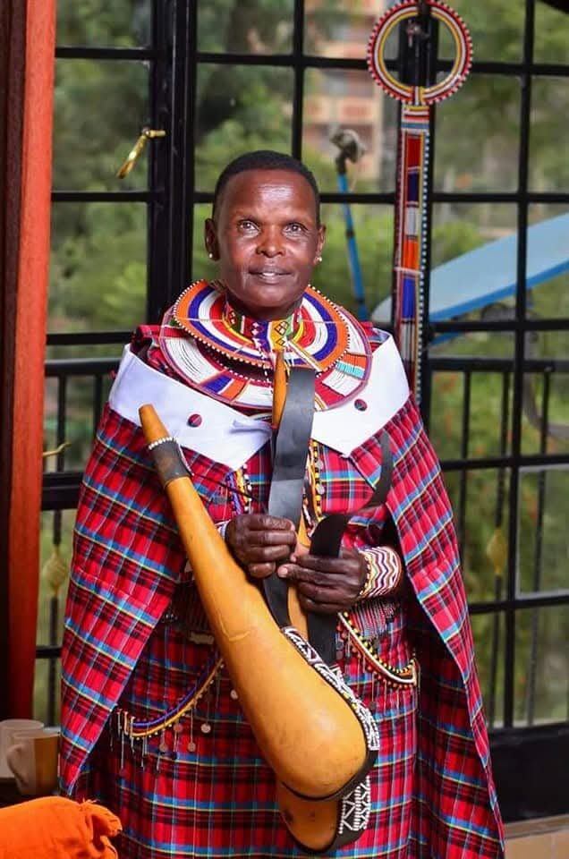 Portrait of a Maasai woman artisan wearing traditional beaded regalia and holding a carved gourd container