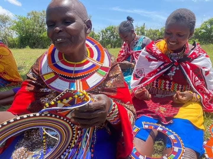 A Maasai elder mentoring a young girl in traditional beadwork in the open grassland