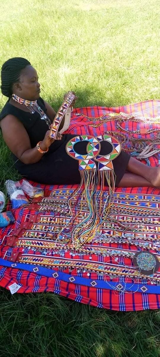 A Maasai woman seated outdoors crafting beaded jewellery
